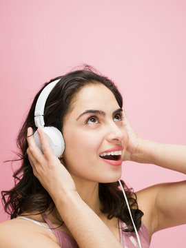 Surprised Brunette Latina Woman Listening To Music With Headphones Against Pink Background