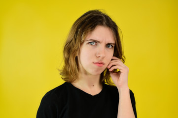 A universal concept, the picture is suitable for any topic. Close-up Studio portrait of a pretty blonde girl in a black T-shirt on a yellow background with bright emotions.