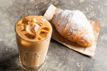 Cold black coffee with ice cubes in tall glass and fresh croissant. Refreshing coffee drink on a...