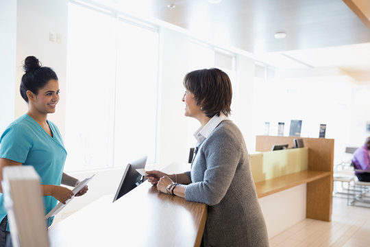 Female Patient Paying Insurance Copay To Nurse With Credit Card At Clinic Check-in Counter