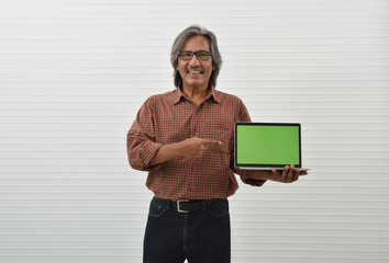 Happy asian senior businessman in red casual shirt and blue jeans holding laptop computer and pointing finger to screen standing over white wall background, Business presentation concept