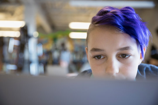 Close up focused pre-adolescent girl with purple hair using laptop