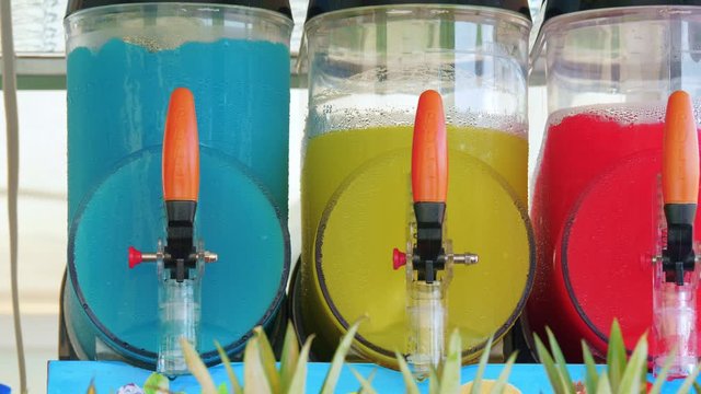 Freezing and mixing machines for making ice slushy drinks containing blue, yellow and red slush. Cold colorful frozen sugar juice.