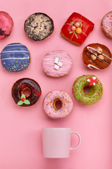 A mug from which sweet donuts fly out, on a pink background. Sweet and coffee donuts concept. colored on pink. Mock up for design. Copy space.