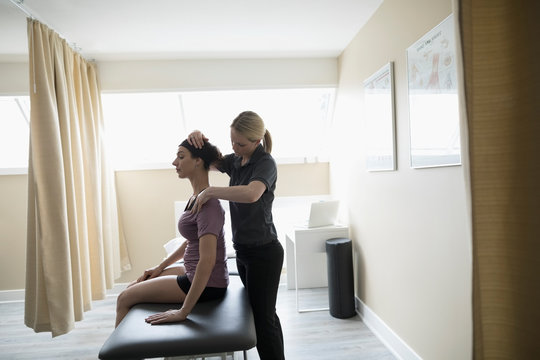 Female physiotherapist stretching neck of client on clinic examination table