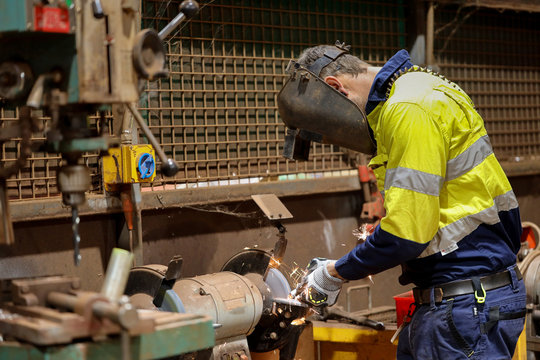 Side picture of miner worker wearing a safety glove eyes protection while using table grinding wheel at the workshop construction site Perth  