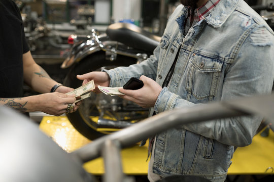 Customer paying motorcycle mechanic with cash in auto repair shop