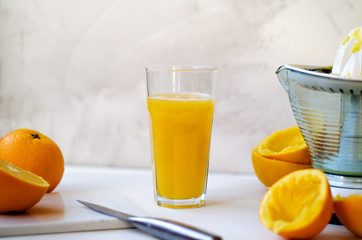 On a wooden table, one whole orange, one cut in half, peel of an orange. On the table lies a stone board and a knife. In the background is a glass cup with freshly squeezed orange juice. On the right