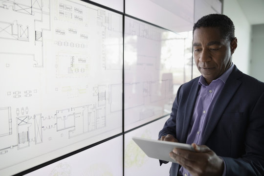 Focused African American Male Architect With Digital Tablet Working At Large Touch Screen In Conference Room