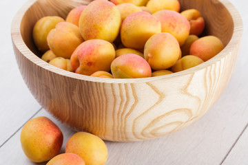 ripe organic apricots fruits in ash tree wooden bowl on a white wooden background