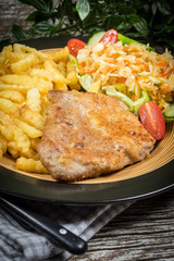 Fried pork chop in breadcrumbs, served with fries and salad.
