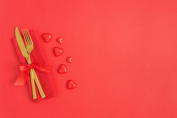 Gold cutlery and heart on red background. Saint Valentines day celebration or romantic dinner minimal concept.