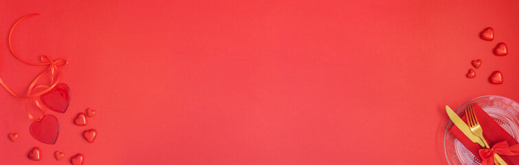 Festive table setting with Gold cutlery and crystal plate, red hearts and gift on red background.Saint Valentines day celebration or romantic dinner concept.