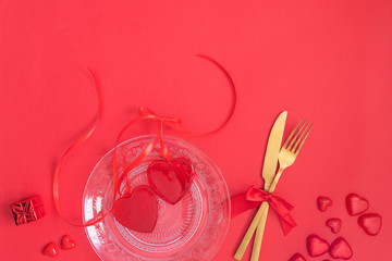Gold cutlery on crystal plate and red heart on red background with monochromatic effect. Saint Valentines day celebration or romantic dinner concept.