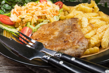 Fried pork chop in breadcrumbs, served with fries and salad.