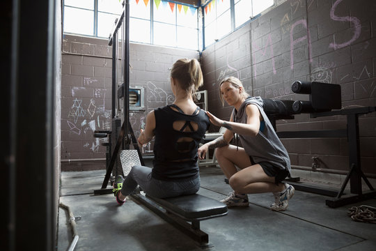 Personal trainer guiding woman weightlifting, doing seated rows in gritty gym