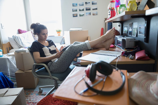 Female College Student With Digital Tablet Studying With Feet Up In Dorm Room