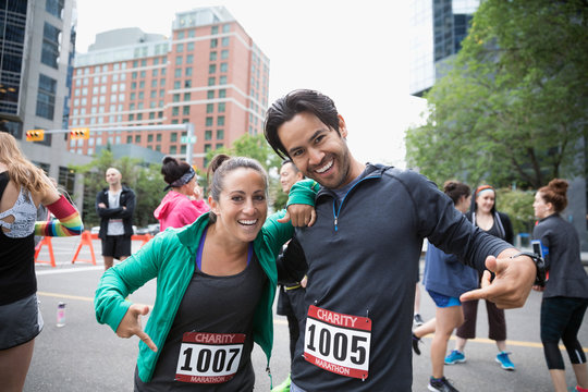 Portrait enthusiastic couple pointing to marathon bibs on urban street