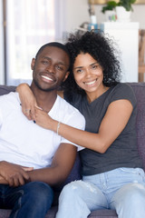 Portrait of happy young black couple posing hugging at couch