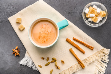 Traditional Indian masala tea chai with milk and spices on napkin on dark stone background with ingredients above
