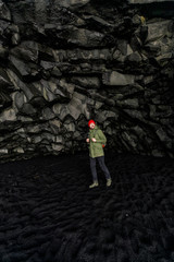 Obraz na płótnie Canvas young male traveler in green clothes in a red hat and a green backpack in a black cave in Iceland