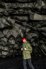 Obraz na płótnie Canvas young male traveler in green clothes in a red hat and a green backpack in a black cave in Iceland