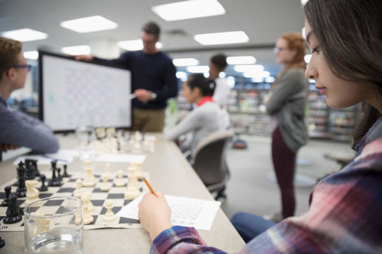 Girl Middle School Student Taking Notes In Chess Club Lesson In Library