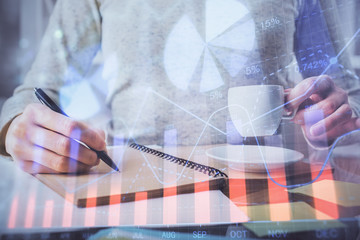 Forex chart hologram on hand taking notes background. Concept of analysis. Double exposure