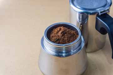 Mokapot coffee brewing with ground coffee beans isolated on brown background.
