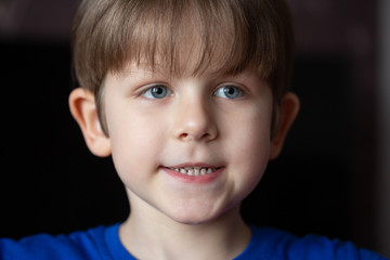 Portrait of a little pretty boy with blond hair close-up on a dark background