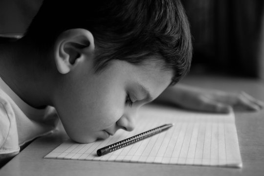 The child,  the schoolboy does not want to do difficult homework, sits at the table, bored. problems with study, concept
