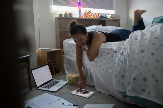 Teenage girl video messaging on digital tablet, doing homework in bedroom