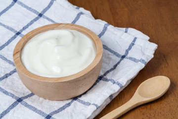 Natural homemade plain organic yogurt in wooden bowl and wood spoon on wood texture background