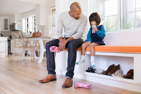 Father Holding Pink Cowboy Boots Next To Toddler Daughter Drinking Juice Box On Window Seat