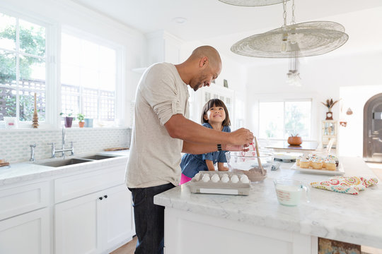 Father and toddler daughter baking cupcakes in kitchen