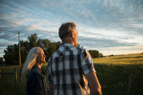 Smiling Couple Farmers Looking At Farm Field At Sunset