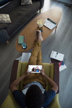 Overhead view teenage boy using digital tablet in living room, looking at photographs