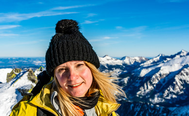 Portrait of a woman with blond hair in a black winter hat with a pom-pom on a background of a winter mountain landscape on a beautiful sunny day.