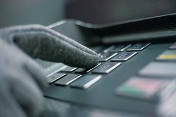 gloved hand enters a pin code on an ATM machine at night