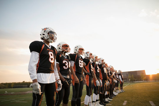 Teenage boy high school football team standing in a row on football field