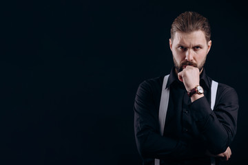 Thoughtful man in black jacket and white suspenders propping up his chin isolated black background...