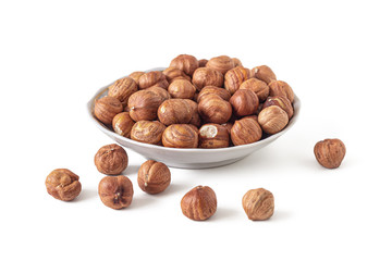 Hazelnuts lie in a small saucer on a white background