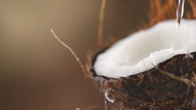 Coconut pouring water, dripping coconut milk, drops of coco nuts oil over brown background. Tropical Coco nut closeup. Healthy Food, skin care concept. Vegan food. 4K UHD video, slow motion