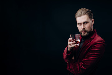 Handsome mature man in vinous jacket with a glass of whiskey toasting and looking at camera isolated black background copyspace