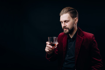 Stylish handsome man in vinous velvet jacket looking at his drink isolated black background copyspace