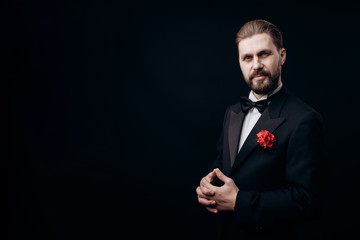 Half-turned handsome man in a dinner suit with a carnation in buttonhole isolated black background copyspace