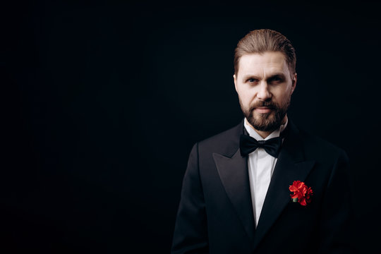Portrait of handsome bearded brunet in black tie with a carnation boutonniere isolated black background copyspace