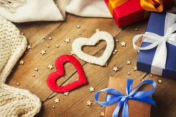 Two hearts, knitted scarf, gift boxes, luminous garland on a wooden background. Concept of lovers, Valentine's Day, a gift for a loved one.