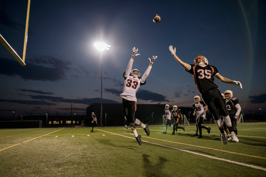 Teenage boy high school football player receiver jumping to catch the ball on football field