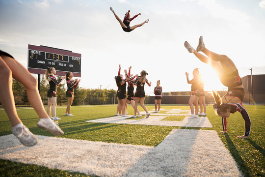 Teenage girl high school cheerleading team performing double nine jump on sunny football field
